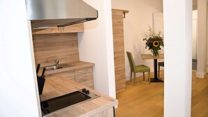 A modern kitchen with a built-in stove, a sink, and wooden cabinetry. There is a dining area with a table and chairs, and a vase with flowers on the table. - Perkeo Apartments: 2 Studios with shared terrace | Heidelberg-Oldtown (Heidelberg)
