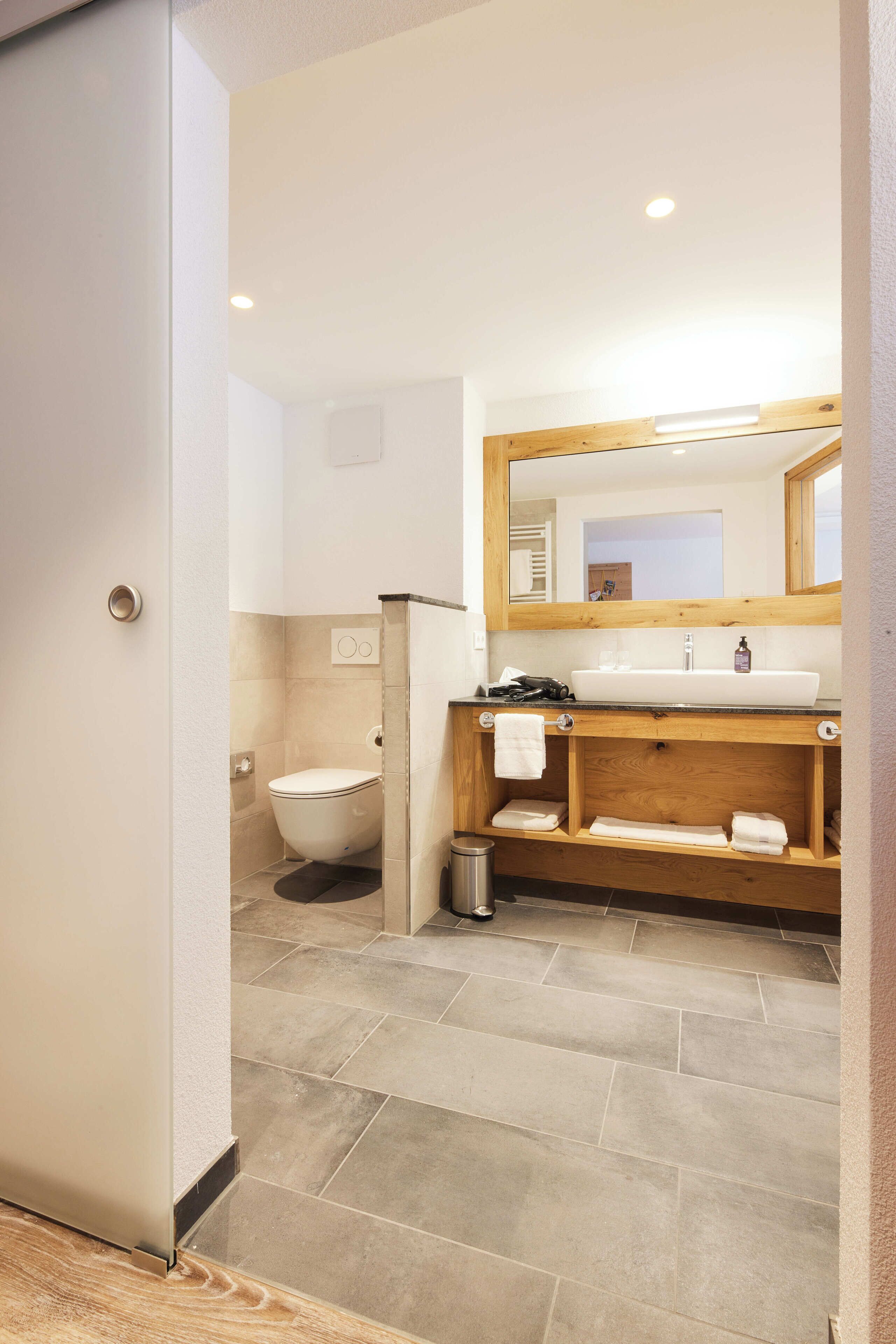 A modern bathroom with a wooden vanity, a white sink, and a mirror above it.