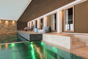 A modern indoor pool area with a stone wall, a wooden slatted ceiling, and a seating area with a table and chairs. - Hotel Sonne-Post (Titisee-Neustadt)