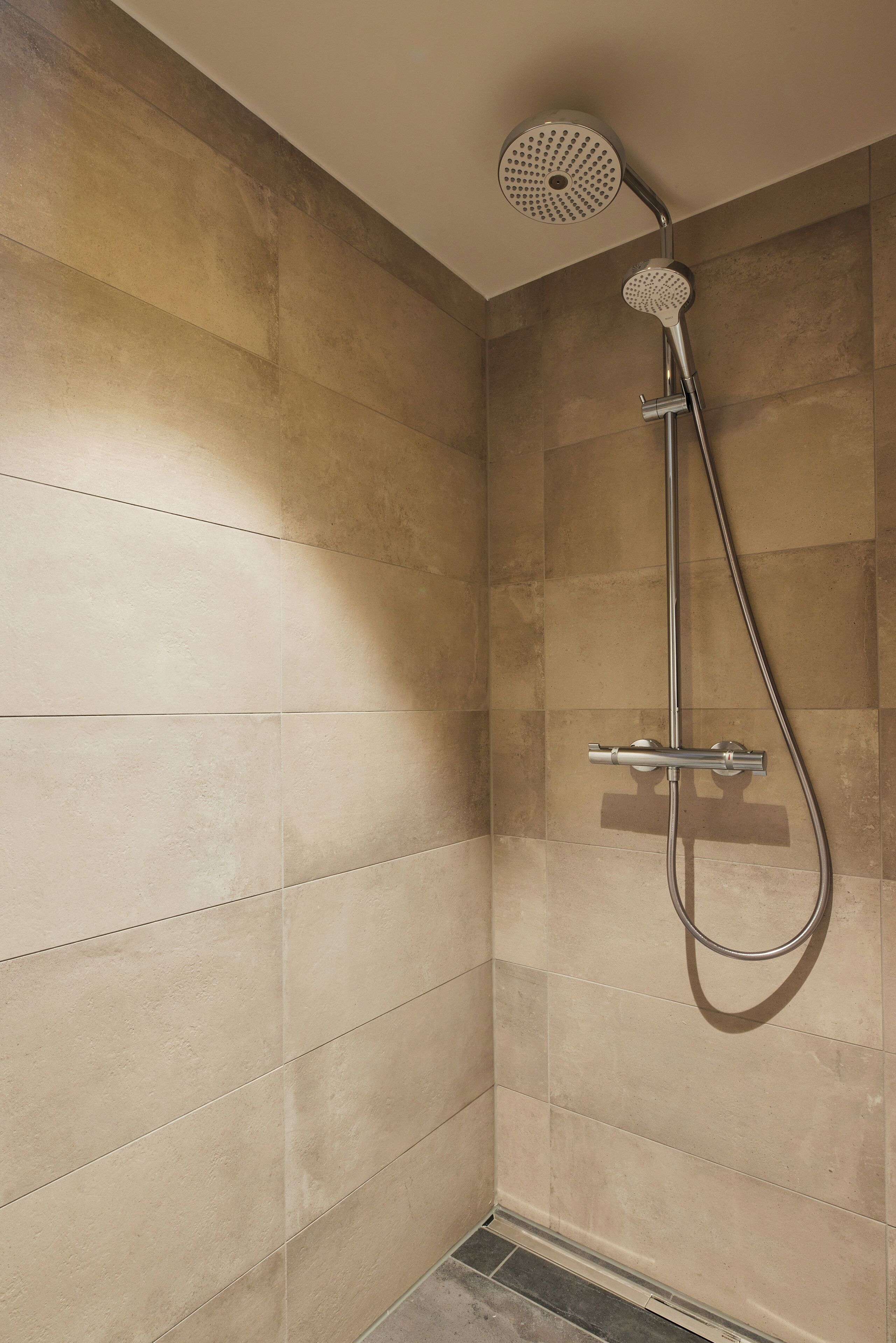 A shower with a handheld showerhead and a wall-mounted control panel.