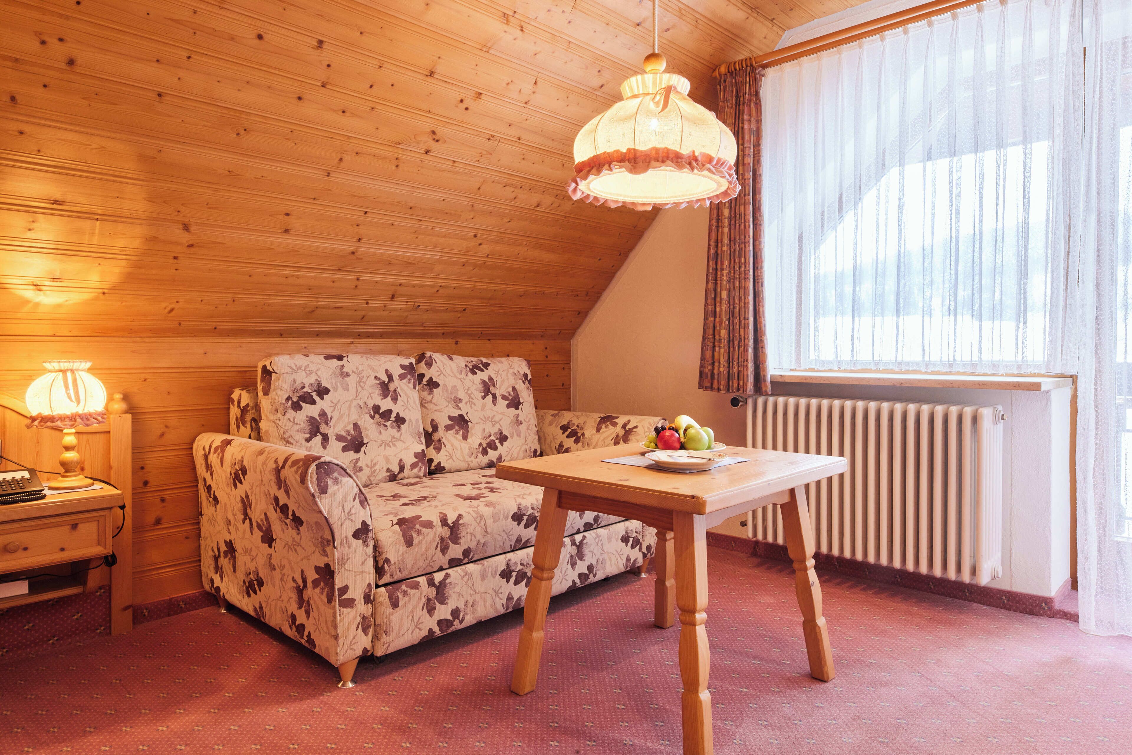Una habitación acogedora con techo de madera, un sofá floral, una mesa de madera con fruta, una lámpara y un radiador.