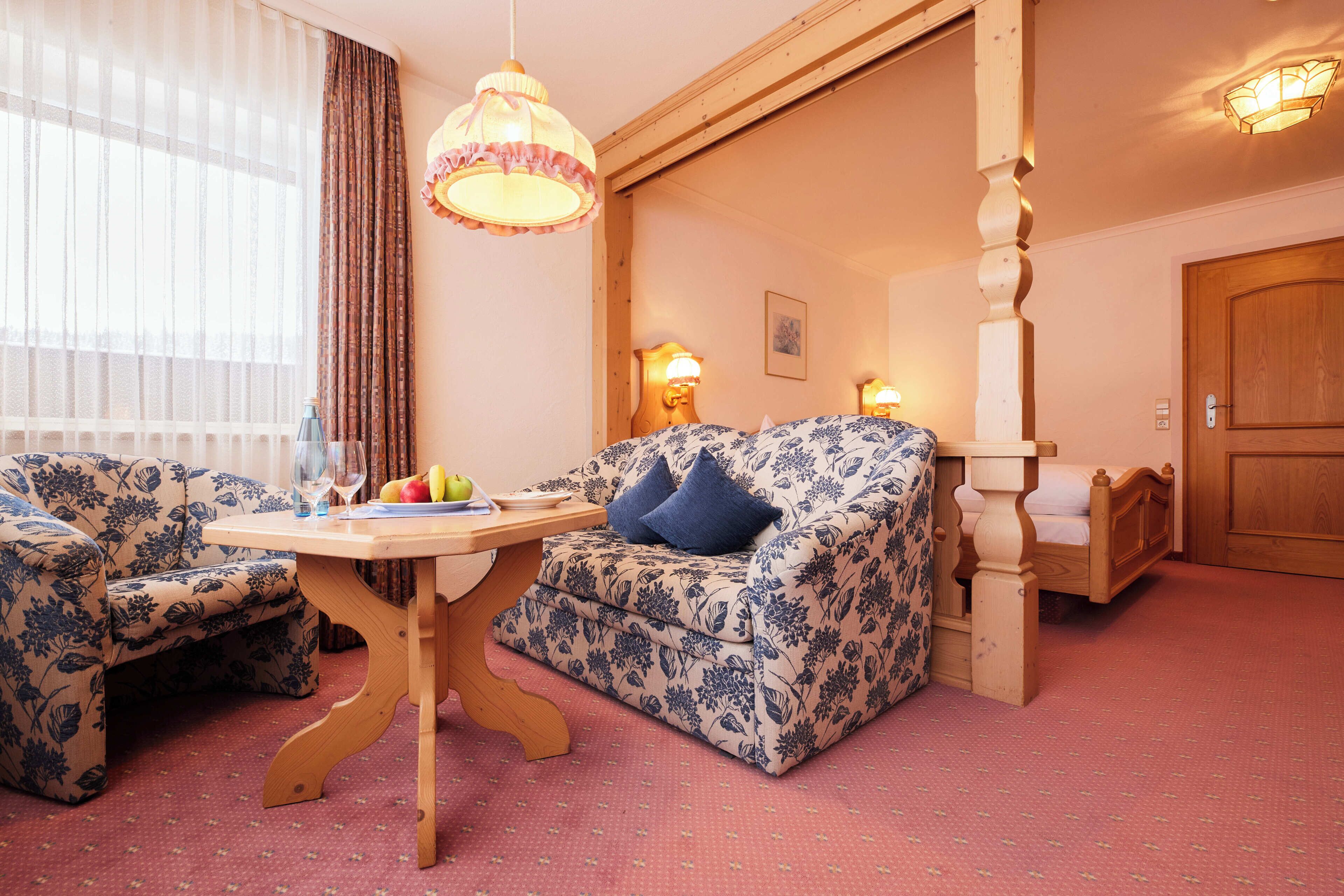 Ein Zimmer mit einem blumigen Sofa, einem Holztisch mit Obstschale und einem hölzernen Bett.