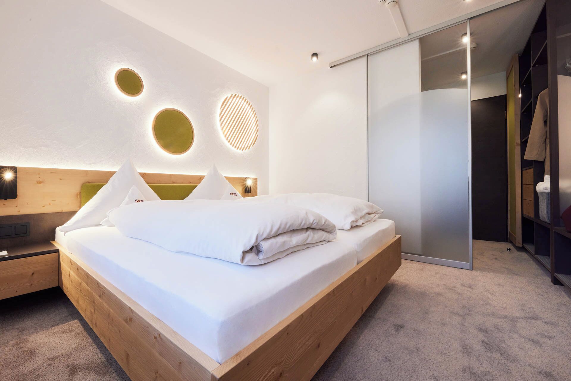 Un dormitorio moderno con una cama de madera, una mesita de noche, una lámpara de pared y un armario con puertas correderas.
