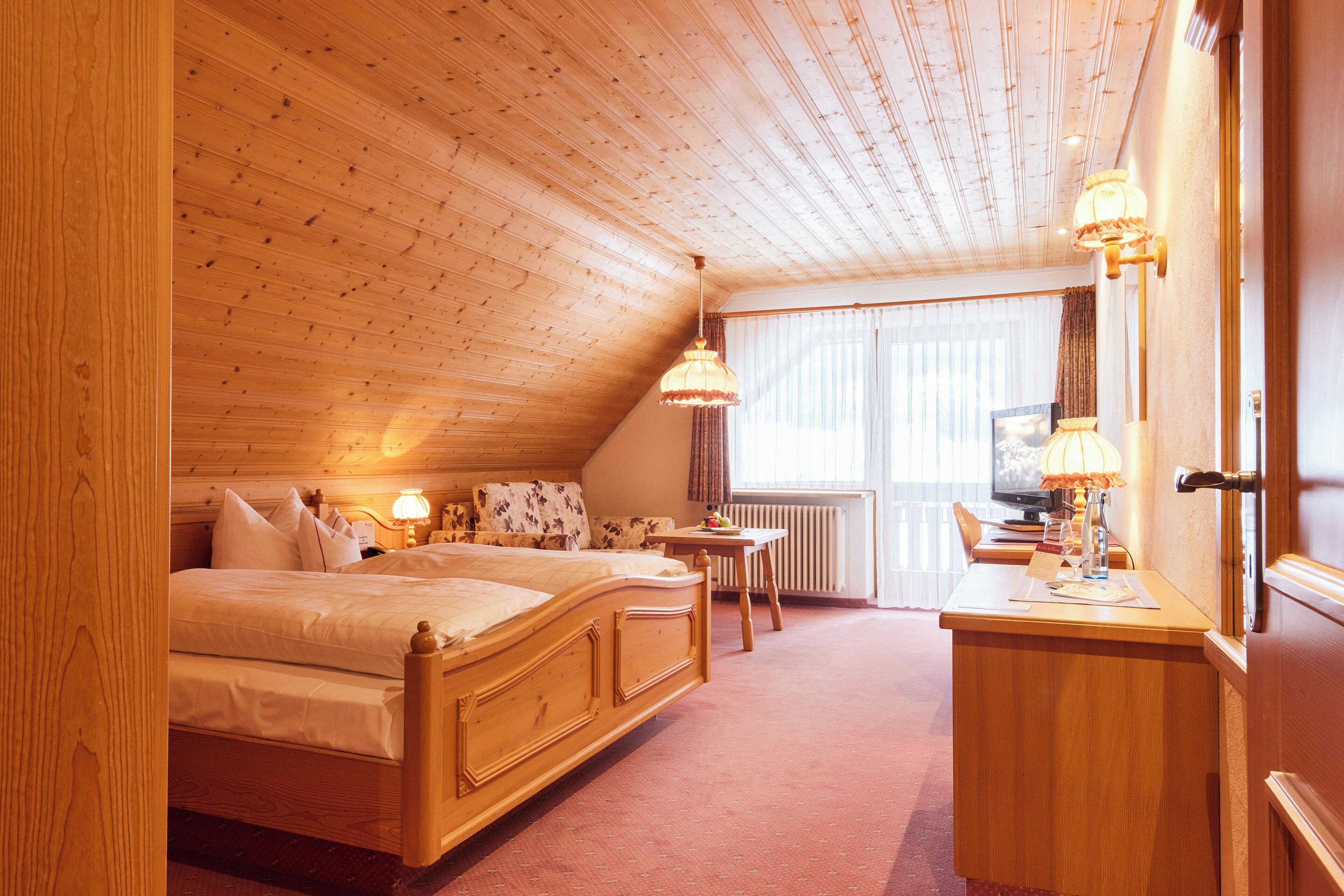 A bedroom with a wooden ceiling, a bed, a desk, and a window with curtains.