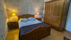 A bedroom with a wooden bed, two bedside tables with lamps, a wardrobe, and a stone wall. - Large house near Paris, garden, for 12 people (Yèvre-la-Ville-Yèvre le Châtel)