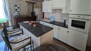 A kitchen with white cabinets, a black countertop, and a dining area with a chair and table. - Large house near Paris, garden, for 12 people (Yèvre-la-Ville-Yèvre le Châtel)