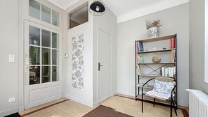 A room with a white door, a bookshelf, a wicker chair, and a radiator. - Charming house in La Ferté-Hauterive, comfort included (La Ferté-Hauterive)