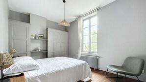 A bedroom with a large bed, a chair, a wardrobe, and a window. - Charming house in La Ferté-Hauterive, comfort included (La Ferté-Hauterive)