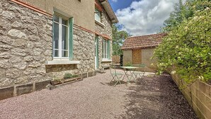 A stone building with a gravel courtyard, a small table with chairs, and a garden wall. - Charming house in La Ferté-Hauterive, comfort included (La Ferté-Hauterive)