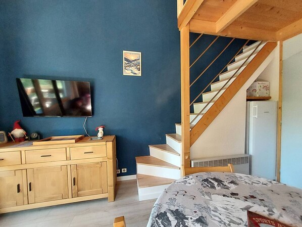 Ein Schlafzimmer mit einem hölzernen Schminktisch, einem Fernseher, einer Treppe und einem Bett mit Blumenmuster.