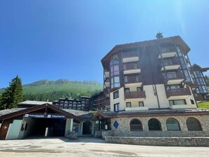 A multi-story hotel with a stone facade, balconies, and a mountain backdrop.