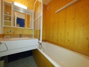 Ein Badezimmer mit Holzwänden, einem weißen Waschbecken und einer Badewanne.
