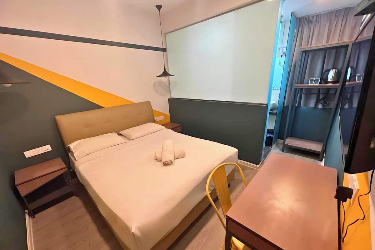 Quarto de hotel com cama, escrivaninha, cadeira e guarda-roupa.