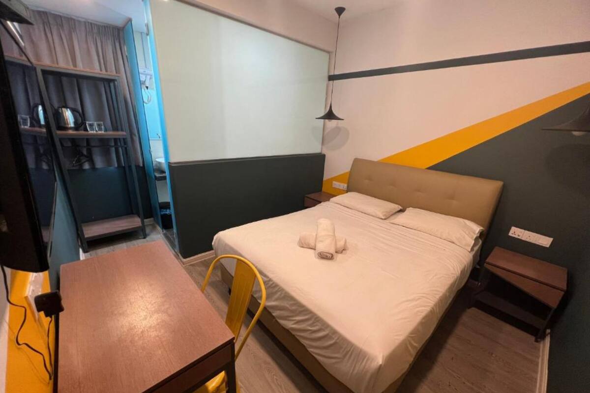 Quarto de hotel com cama, escrivaninha, cadeira e guarda-roupa.