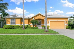 A residential house with a garage, a well-maintained lawn, and palm trees.