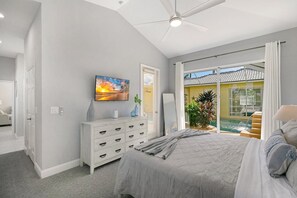 A bedroom with a bed, a dresser, a painting, and a view of a pool.