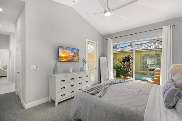 A bedroom with a bed, a dresser, a painting, and a view of a pool.