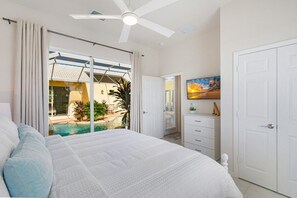 A bedroom with a bed, a ceiling fan, a sliding glass door leading to a pool, and a white wardrobe.