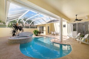 An indoor swimming pool with a glass ceiling, surrounded by lounge chairs and a small hot tub.