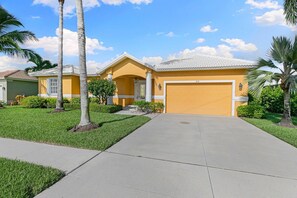 A residential property with a yellow facade, a garage, and a well-maintained lawn with palm trees.