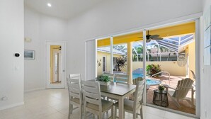 A dining area with a table and chairs, a view of a swimming pool, and a door leading to another room. - The Sandbar - 3BDR Courtyard Home w/Pool & Spa (Marco Island)