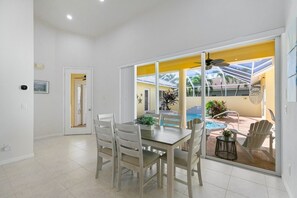 A dining area with a table and chairs, a view of a swimming pool, and a door leading to another room.