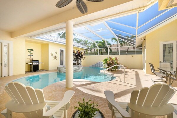 An indoor swimming pool with lounge chairs, a grill, and a covered patio area.