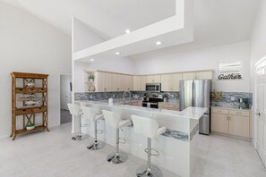 A modern kitchen with a central island, bar stools, and a 'Gather' sign on the wall.