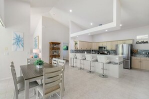 A modern kitchen with a central island, bar stools, and a dining area with a table and chairs.