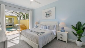A bedroom with a bed, bedside tables, a ceiling fan, a painting, and a view of a pool and outdoor area. - The Sandbar - 3BDR Courtyard Home w/Pool & Spa (Marco Island)