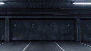 Un garaje de estacionamiento vacío con paredes y pisos de concreto, espacios de estacionamiento delimitados e iluminación fluorescente.