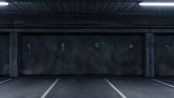 An empty parking garage with concrete walls and floors, marked parking spaces, and fluorescent lighting.