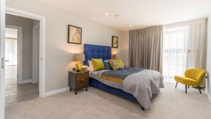 Un dormitorio con una cama grande, mesitas de noche, una silla y cortinas.