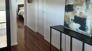 Un corridoio con pavimento in legno, pareti bianche e un grande quadro astratto su un supporto nero.