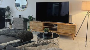 Un soggiorno moderno con un'ampia TV a schermo piatto, uno specchio rotondo e un mobile TV in legno.