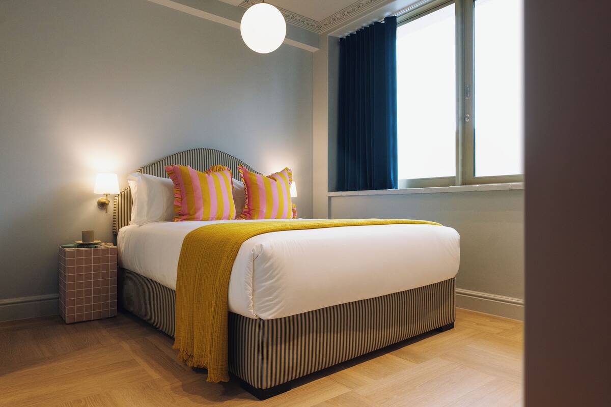Een moderne slaapkamer met een groot bed, een nachtkastje, een lamp en een raam met gordijnen.