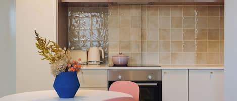 A modern kitchen with a round white table, pink chairs, and a blue vase with flowers.