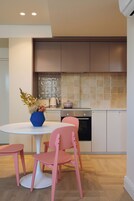 A modern kitchen with a round white table, pink chairs, and a blue vase with flowers.