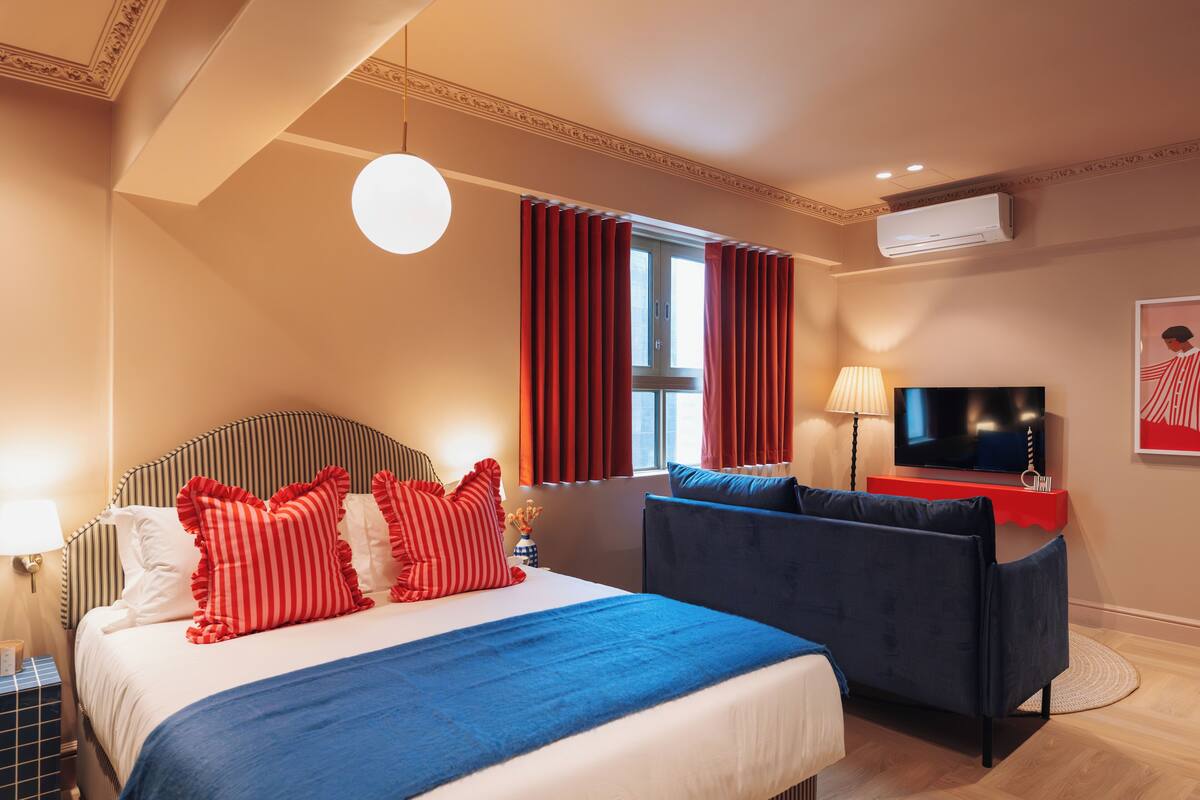 Een hotelkamer met een bed, een bank, een televisie en een raam met gordijnen.