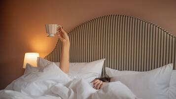 A person lying in bed with a cup in hand, a striped headboard, and a bedside lamp.