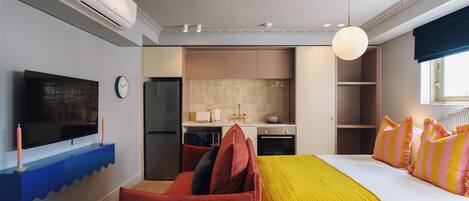 A modern hotel room with a large bed, a TV, a kitchen area, and a bathroom.