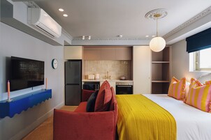A modern hotel room with a large bed, a TV, a kitchen area, and a bathroom.