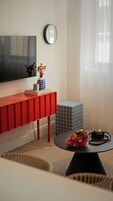 A modern living room with a red console table, a black coffee table with flowers, a vintage camera, and a large flat-screen TV.