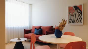 A modern living room with a red sofa, orange chairs, a white table, and a painting on the wall.