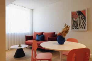 Una sala de estar moderna con un sofá rojo, sillas naranjas, una mesa blanca y un cuadro en la pared.