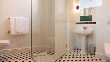 A bathroom with a glass-enclosed shower, a white sink with a gold faucet, and a toilet. The floor has a black and white checkered pattern.