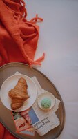 A tray with a croissant, a small green pastry, and a newspaper on a table.