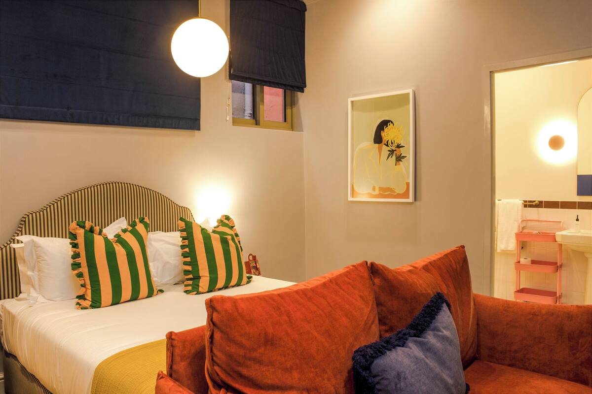 Hotelkamer met een bed, een bank, een schilderij en een badkamer met een wastafel en spiegel.