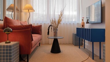 A modern living room with a sofa, a round coffee table, a lamp, a vase with dried plants, and a blue console table.