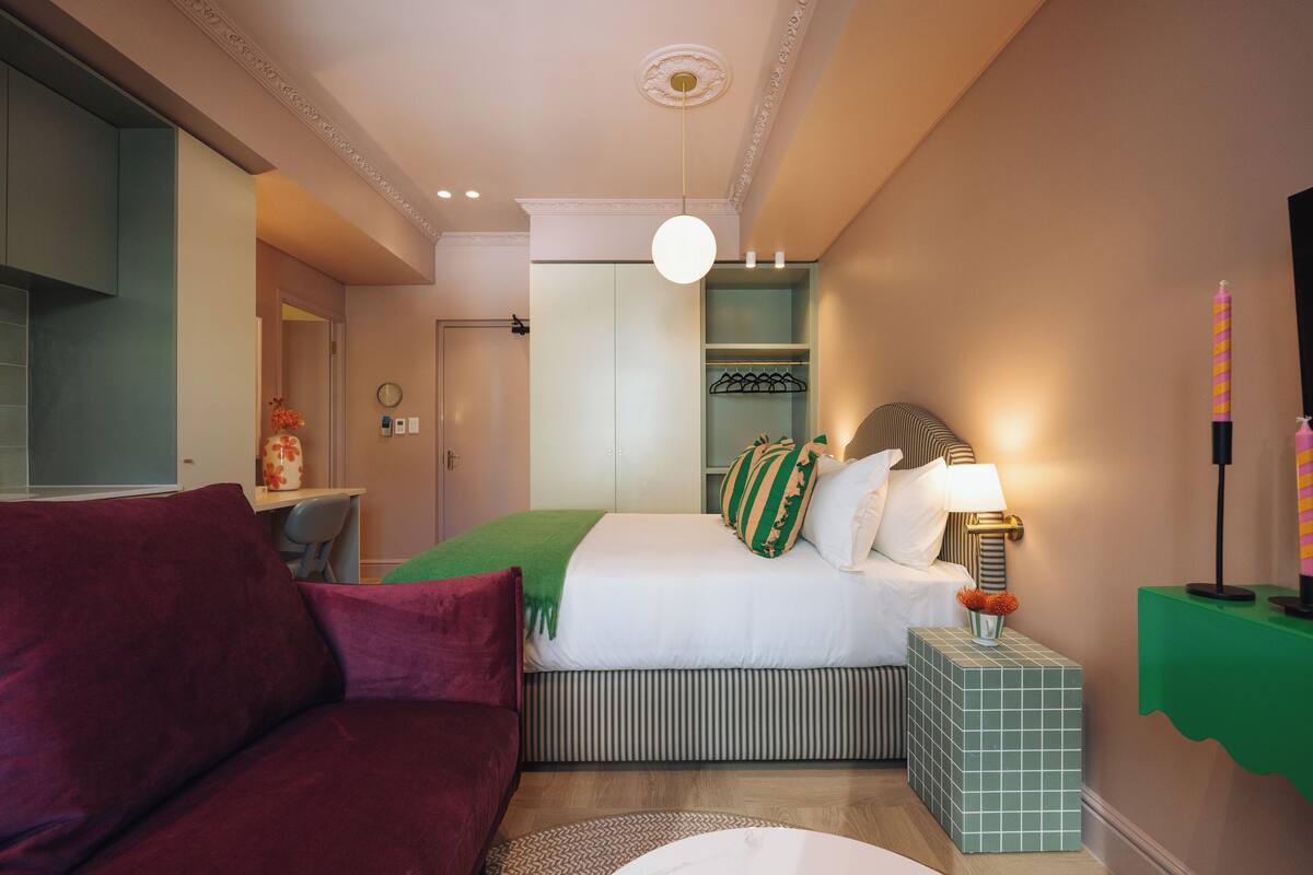 Een hotelkamer met een bed, een slaapbank, een nachtkastje, een lamp en een groene bijzettafel.